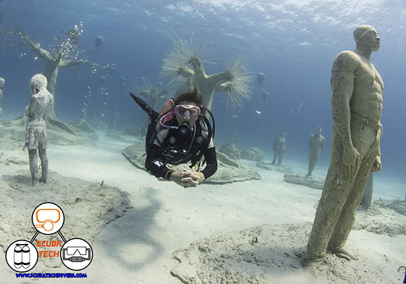 A diver poses in front of the scultured trees and figures in the MUSAN museum of underwater scultures in ayia napa