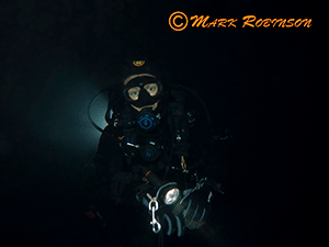 diver scuba diving and night with torch and backlit by another diver